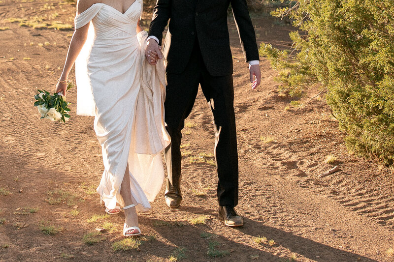 closely cropped image of a bride and groom holding hands while walking