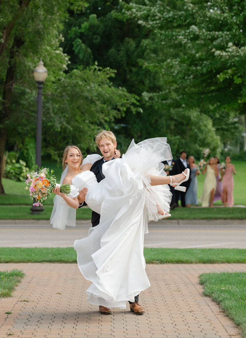 A groom picks up his bride in front of their wedding party in Michigan