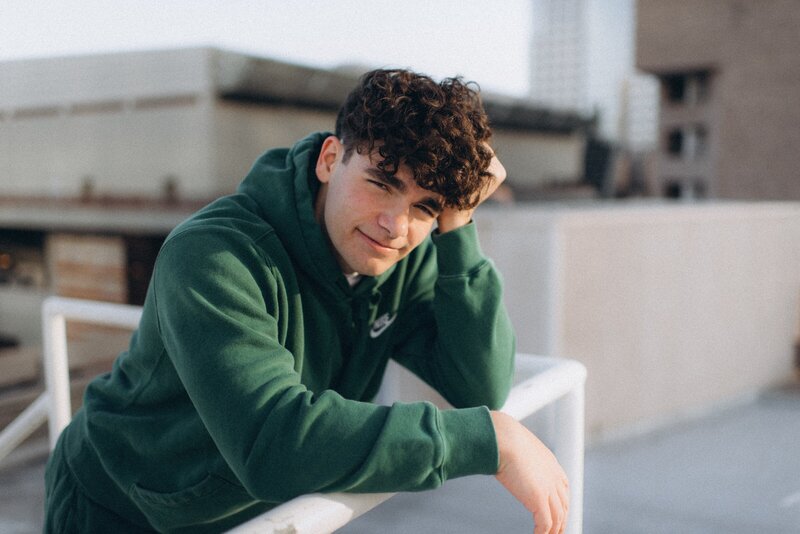High school senior boy is leaning on a railing looking at the camera in Scottsdale