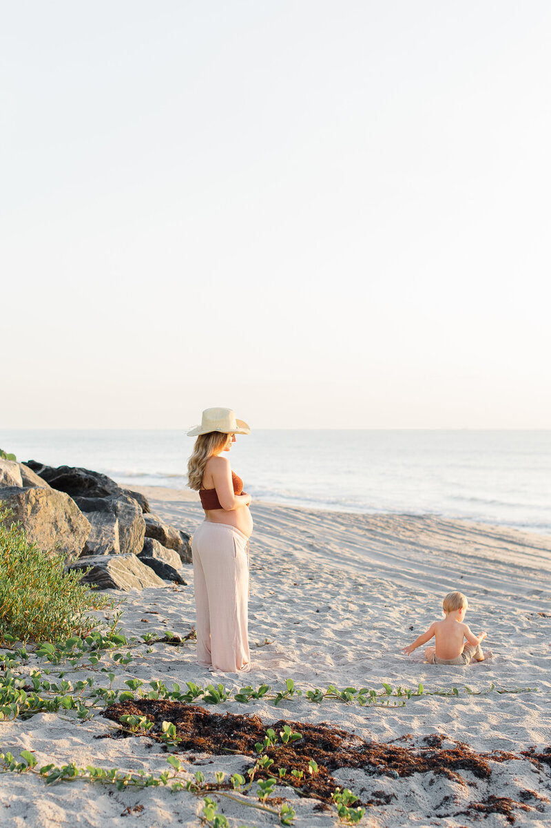 Beautiful pregnant mother watching her son play in the sand at sunrise documented by a Central Fl photographer