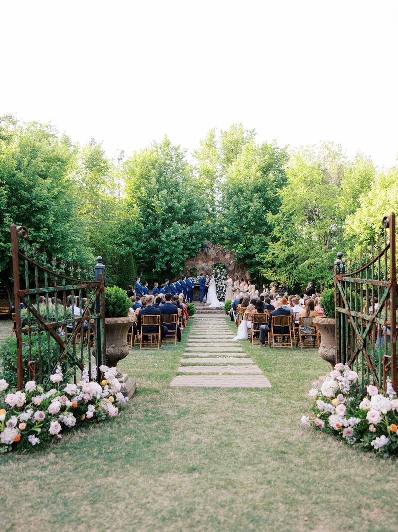 ceremony picture with iron gates and flowers and guests and ceremony in background at Stone Chapel in Fayetteville, Arkansas