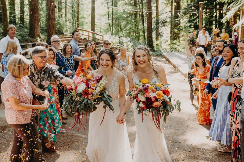 couple stands in midst of brush and tumbleweed smiling and embracing
