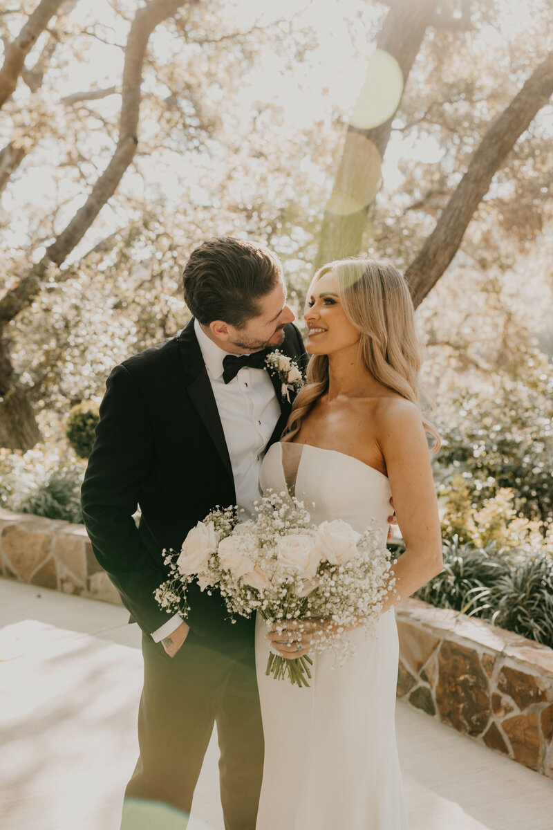 Bride holding a bouquet of roses and baby’s breath smiling at her groom during their Long Beach wedding, coordinated with month-of services by Beyond the Event and photographed by Kellie Jane Photography