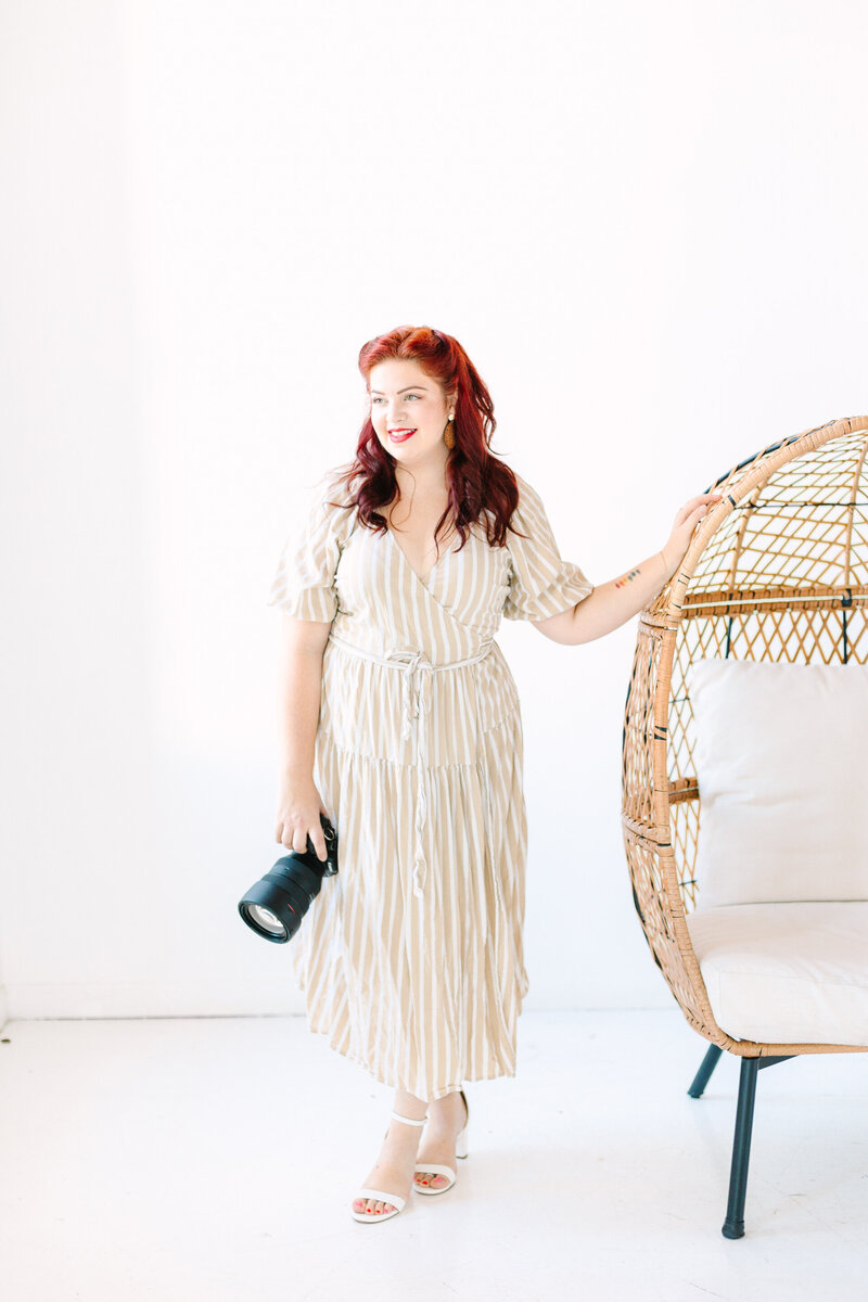 Portrait of Lelia Angelique, a wedding photographer, standing with a camera in hand and smiling in a bright, airy setting.