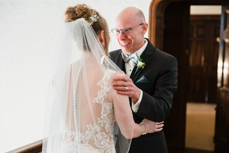 The wind picks up the light fabric of a brides train while standing in front of a windmill and embracing her new husband for a kiss and holding a beautiful neutral colored bouquet.