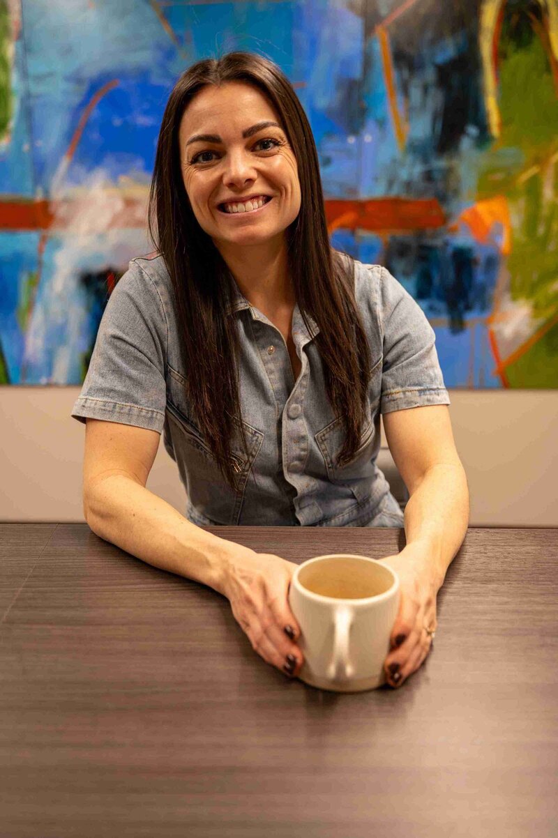A Denver-based Functional Nutritionist sits at a table, savoring a cup of coffee while contemplating her next steps.