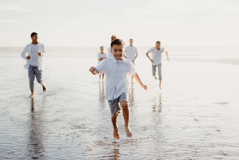 A little boy running in the water at the beach being photographed by Family Photographer Tashina Narelle in Auckland