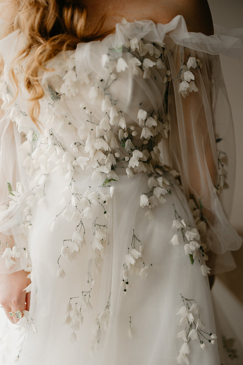 Below the waste close up of bride and groom holding hands and bouquet