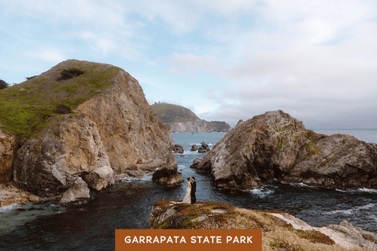 A couple stands on a coastal bluff at Garrapata State Park, surrounded by rugged cliffs and ocean views.