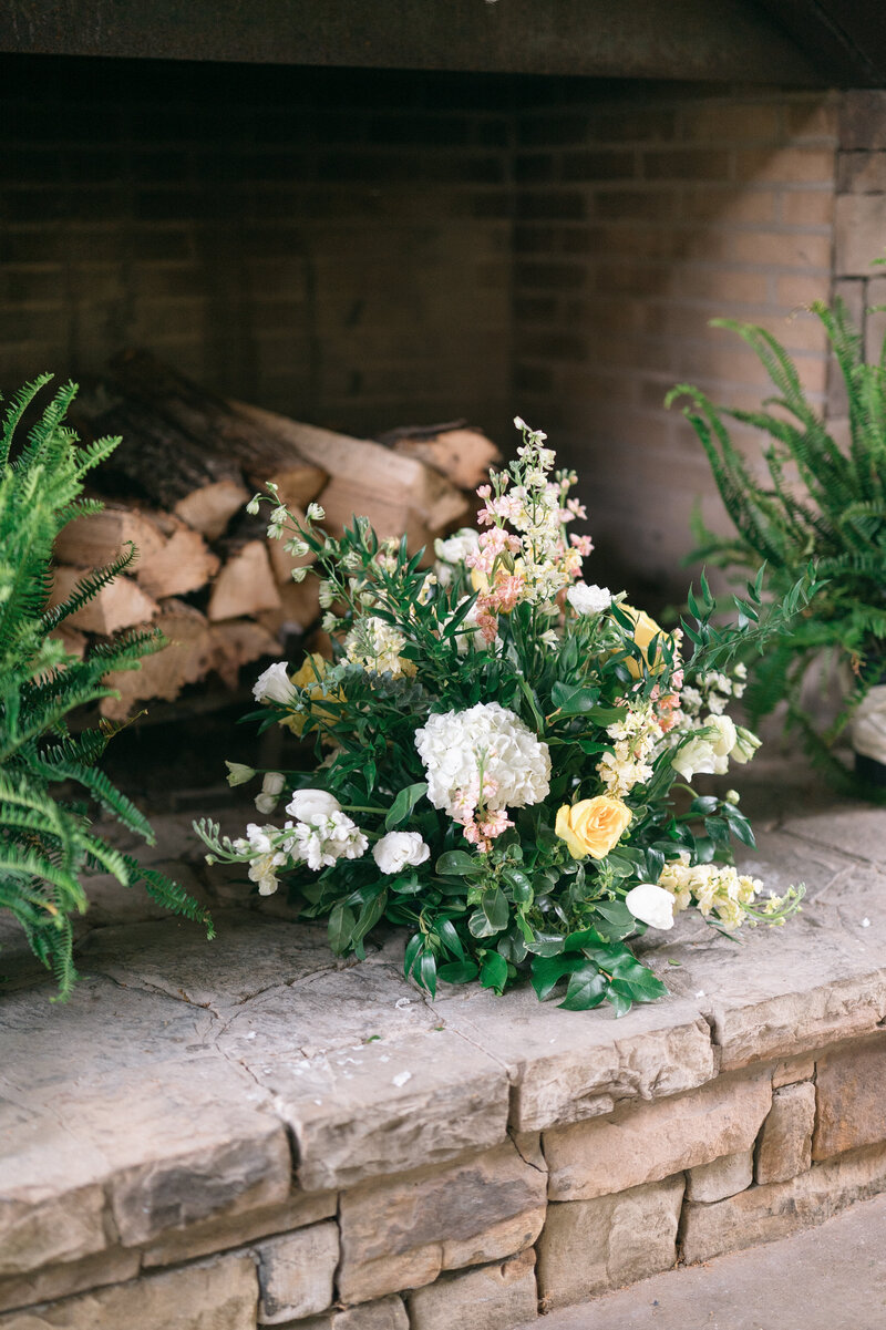 Greenery with white and yellow flowers in front of a stone fireplace