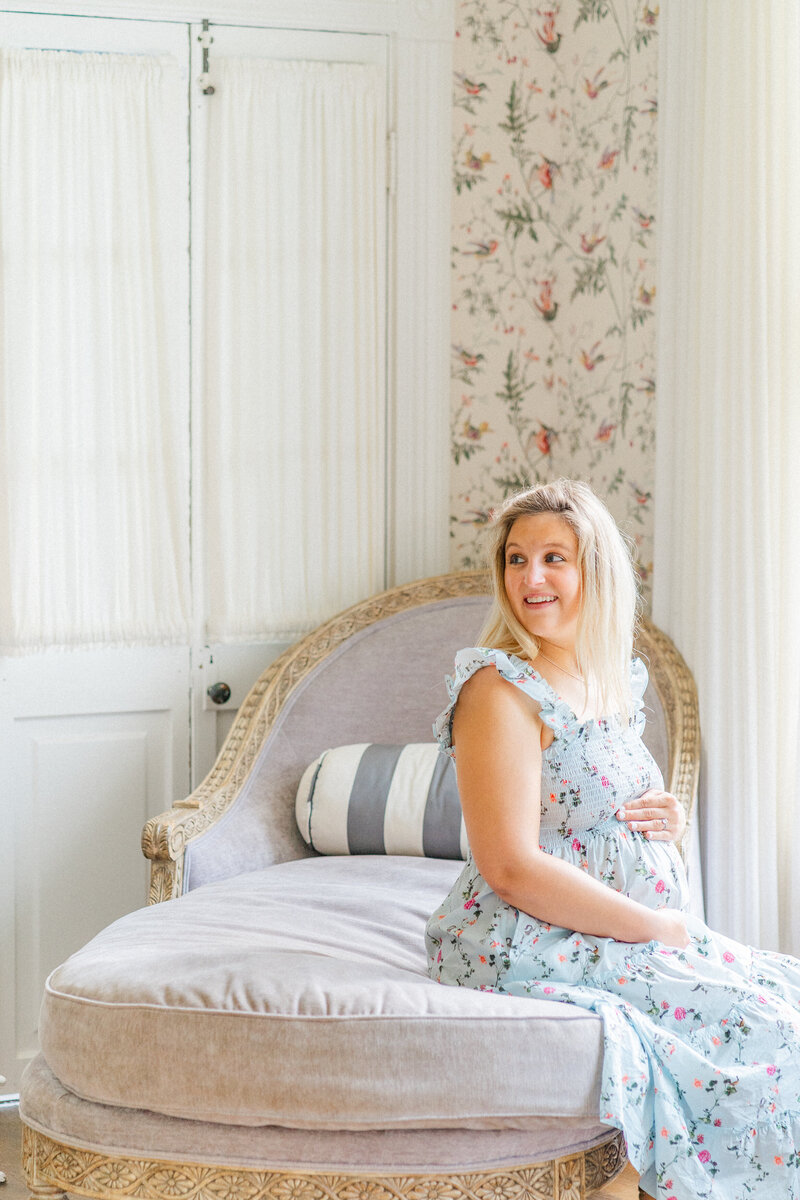 Austin Maternity Photographer | A pregnant mother in a floral dress sits on a daybed at Woodbine Mansion in Round Rock