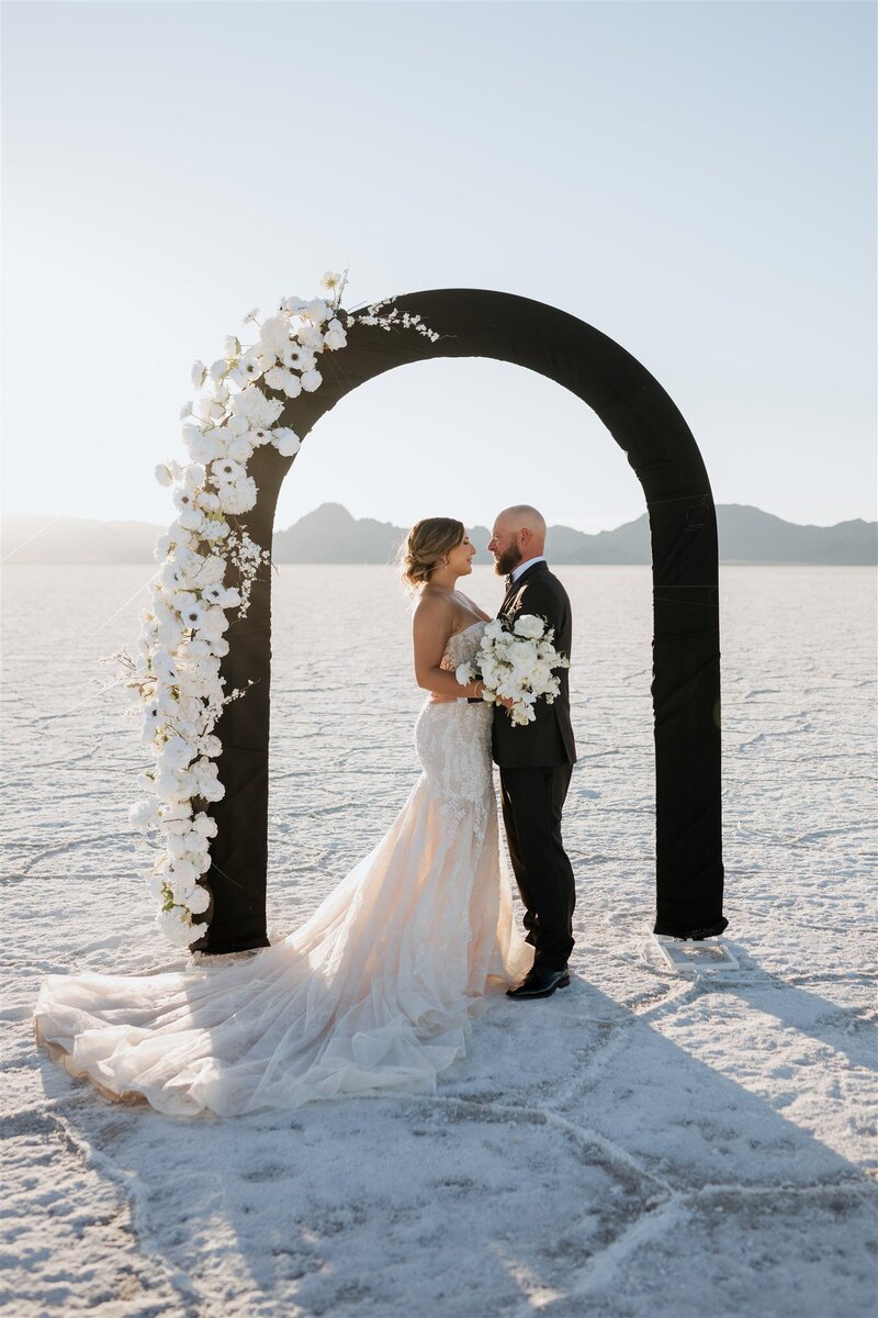 Couple under a beautiful arch with the sunset in the background of their salt flats elopement.