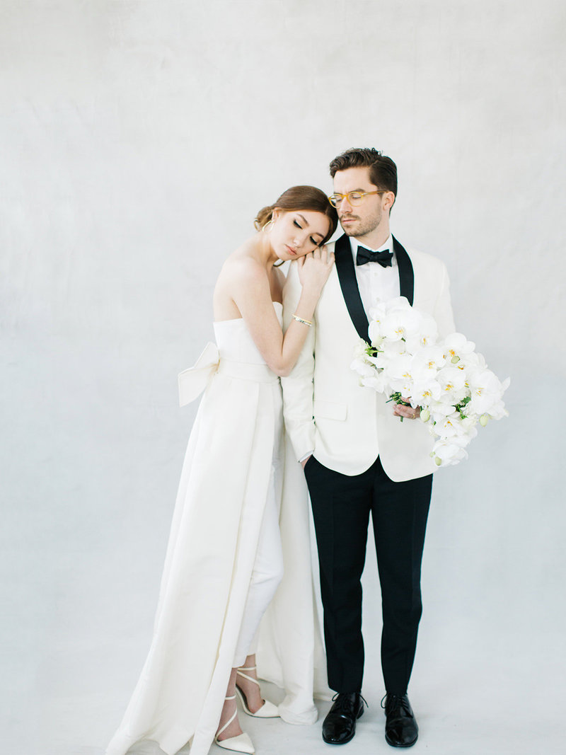 A destination wedding couple in wedding dress jumpsuit with  removable cape and dinner jacket