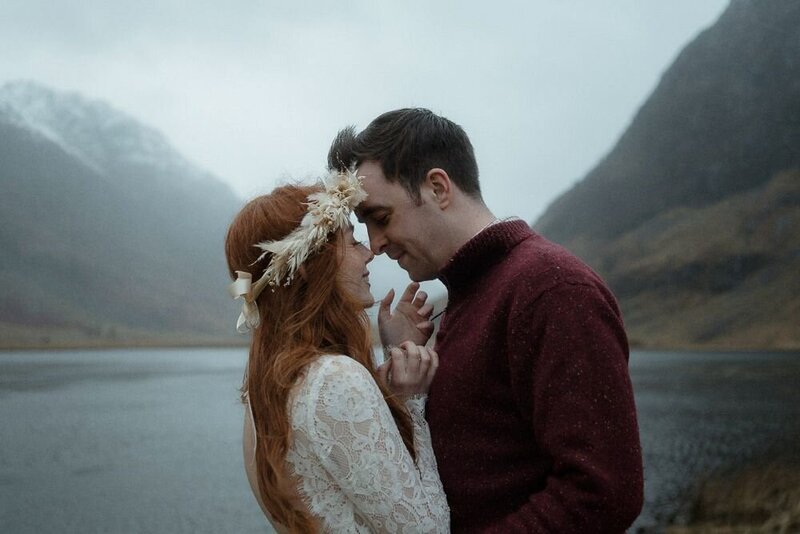 Bride and groom kiss by a loch on a wet and stormy day during their elopement in Glencoe, Scotland