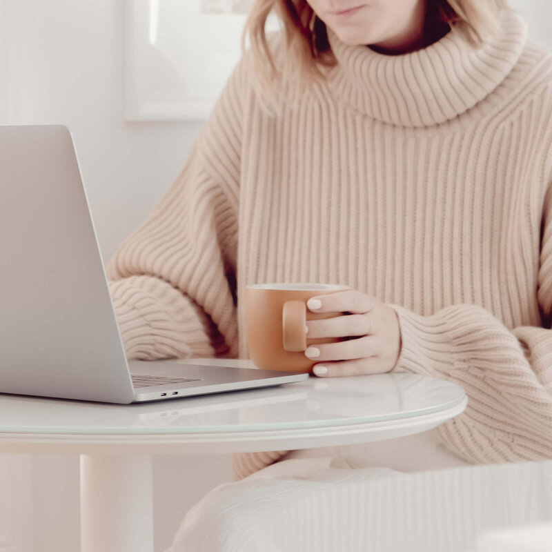 woman sitting at table drinking  coffee and working on her laptop