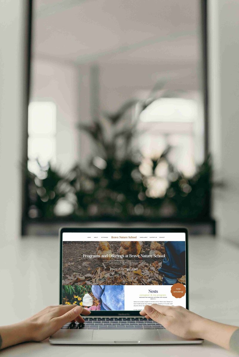 A woman sits at a desk, using a laptop to explore forest school website design homepage.