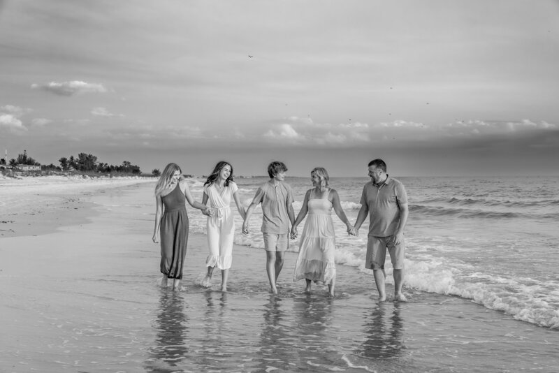 Family of five walking along the waterline on the beach. black and white.