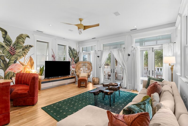 Spacious living room with large TV, peacock chair, and colorful flamingo mural at The Florida House in Carillon Beach, close to 30A and Santa Rosa Beach.