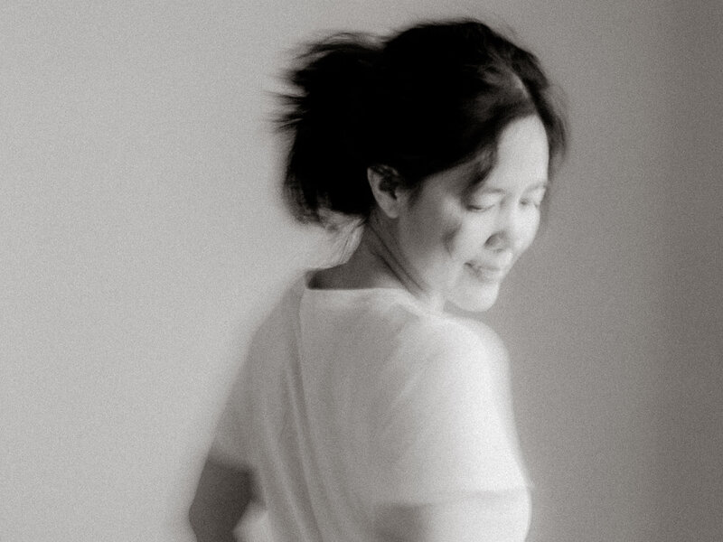 Soft black and white self-portrait of Canyon Lake newborn photographer Jess Young, captured in motion to reflect the gentle, fleeting rhythm of motherhood and the heart behind her in-home sessions.