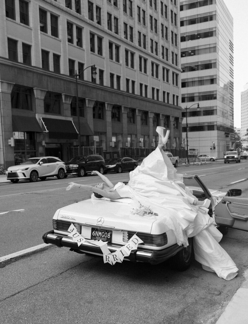 a stylish bride lays on vintage mercedes wedding convertible, hands in the air in celebration before State Savings Bank Detroit wedding