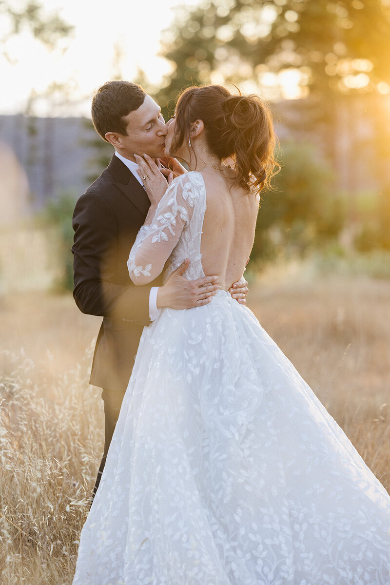 Bride and groom kissing while groom hold bride by her wait in white dress
