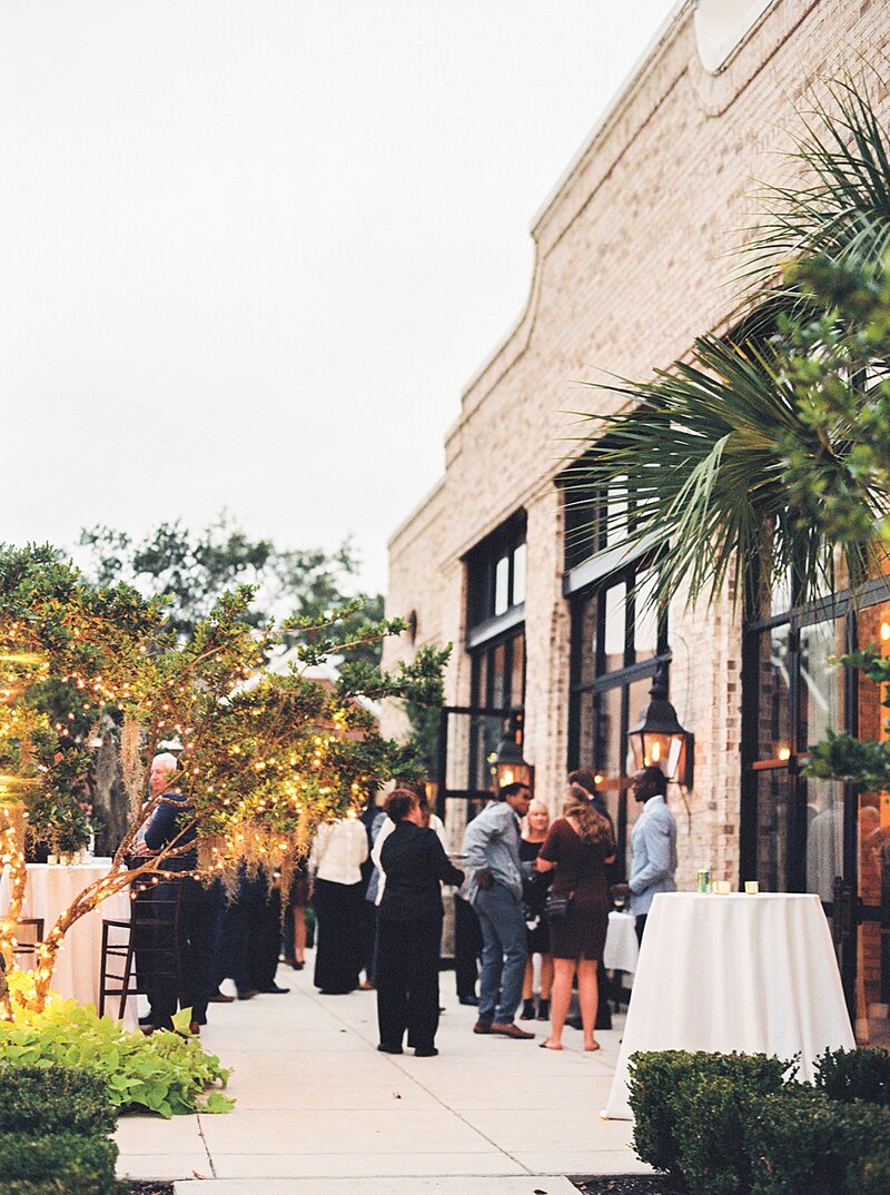 Evening wedding cocktail hour at Wrightsville Manor in Wilmington NC, with brick facade, palms, and glowing string lights