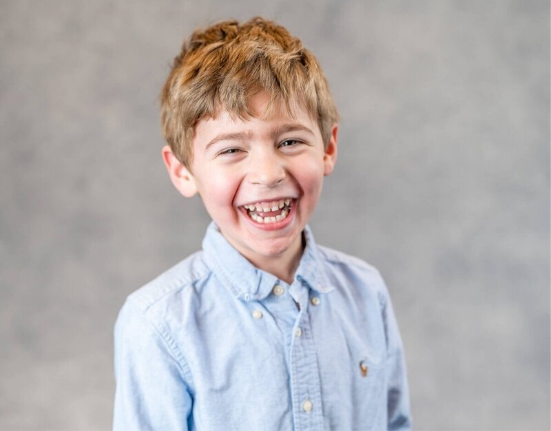A child smiles in a blue button up shirt.