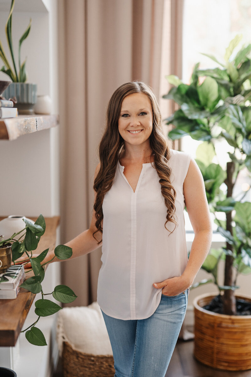 Portrait of woman standing next to shelf with plant and books