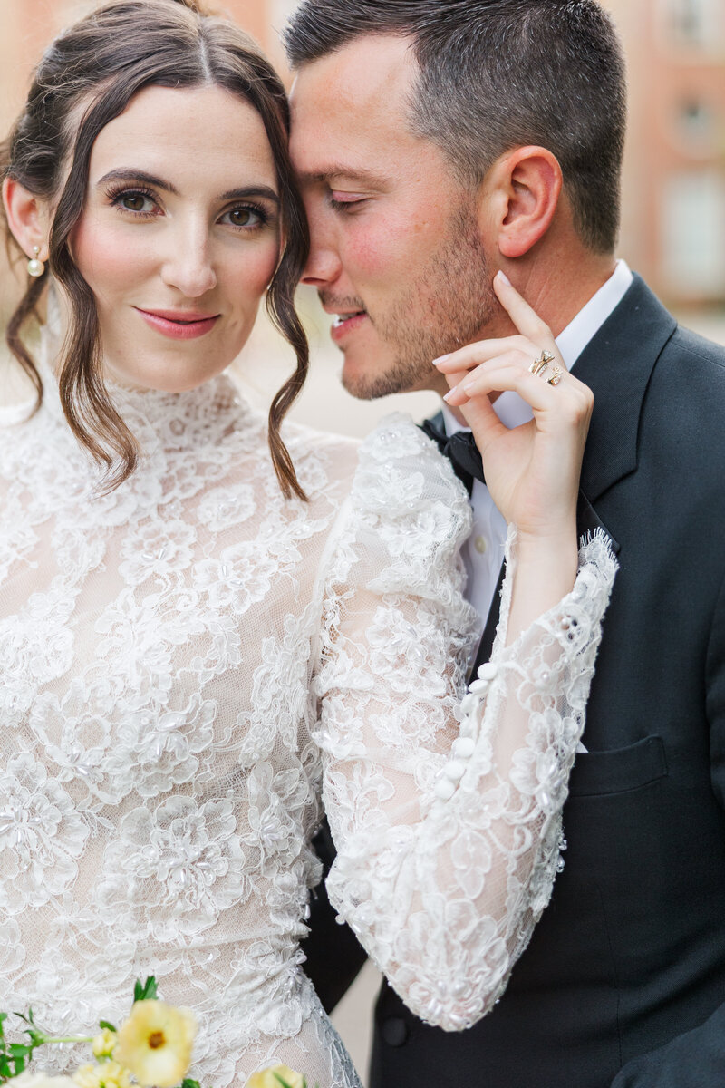 bride stands in front of groom and takes her hand and places it on his cheek as he turns his face toward his smiling
