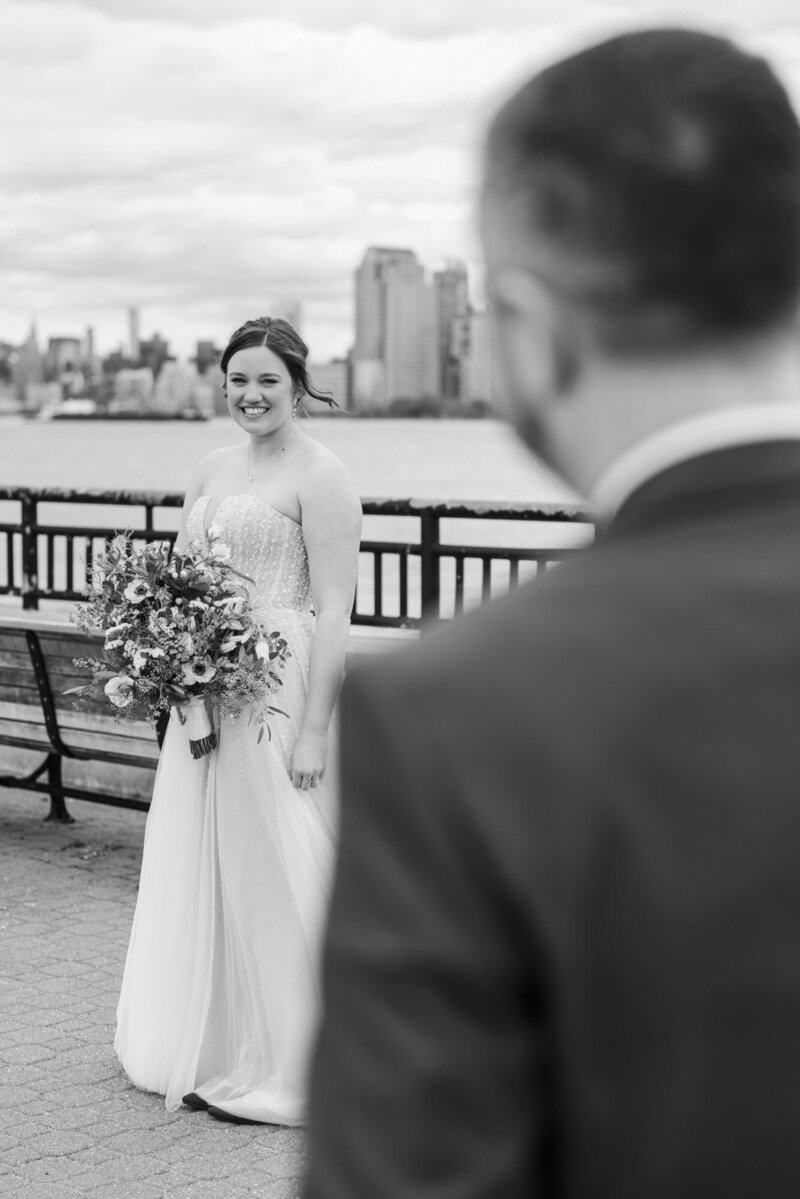 Jessica smiling at Matthew during their wedding day first look on the Hudson River waterfront, in black and white