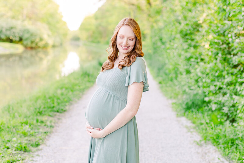 a pregnant woman smiling while standing on a nature trail