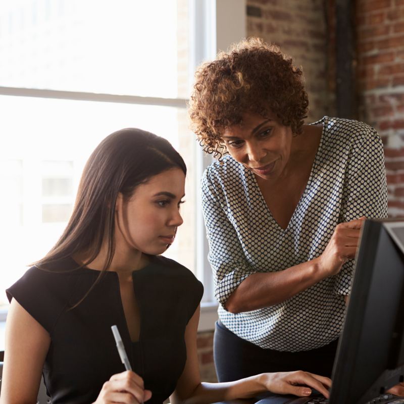 A woman appearing to teach a young girl, looking at a computer together