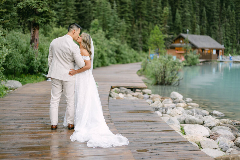 This romantic image shows the bride and groom sharing a kiss by the serene shoreline of Lake Louise. The tranquil waters and picturesque setting create a perfect backdrop for this intimate moment.