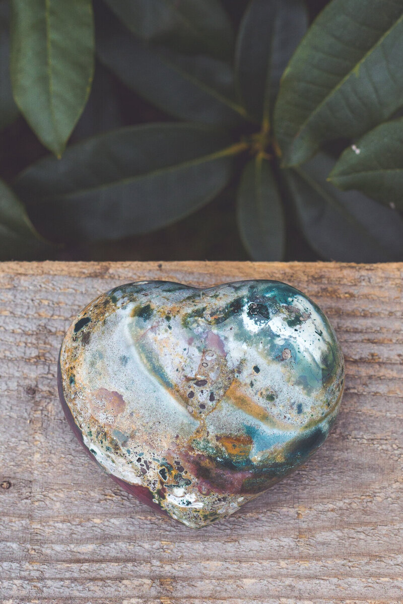 The front side of a moss agate heart crystal with green and burgundy colours.