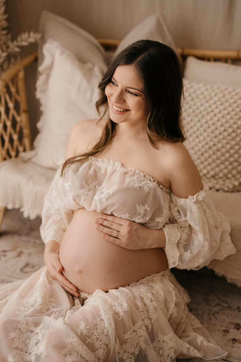 Photo of a pregnant woman wearing a lace dress and skirt smiling during a maternity photography photoshoot.