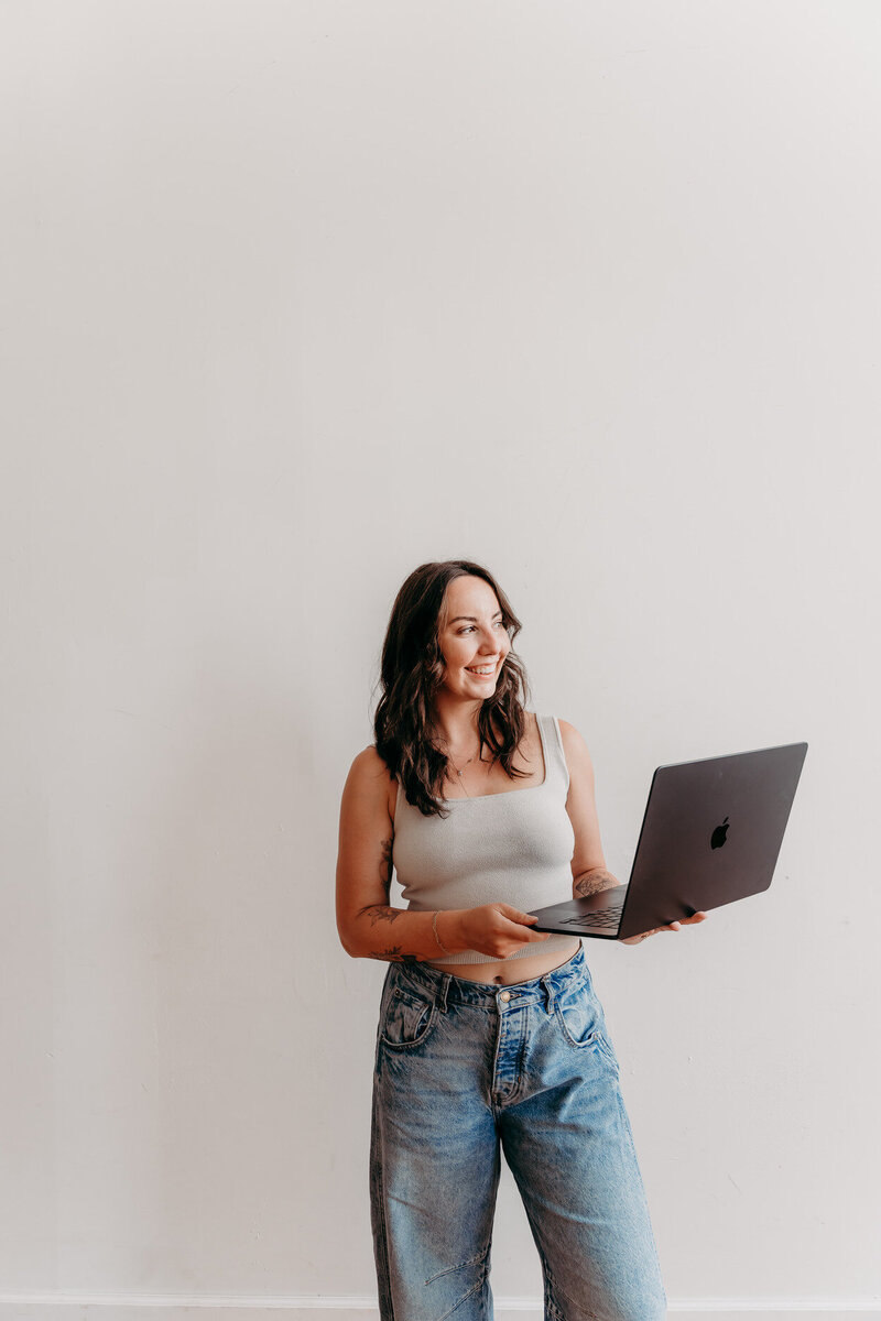 Delia, copywriter, looking outside in a studio space, holding her laptop up during a brand photoshoot.