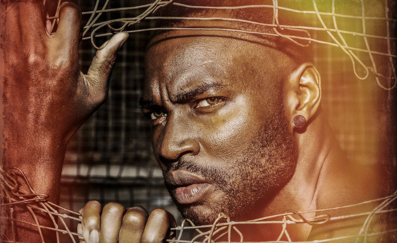 musician portrait Don Castor closeup peering through metal fence