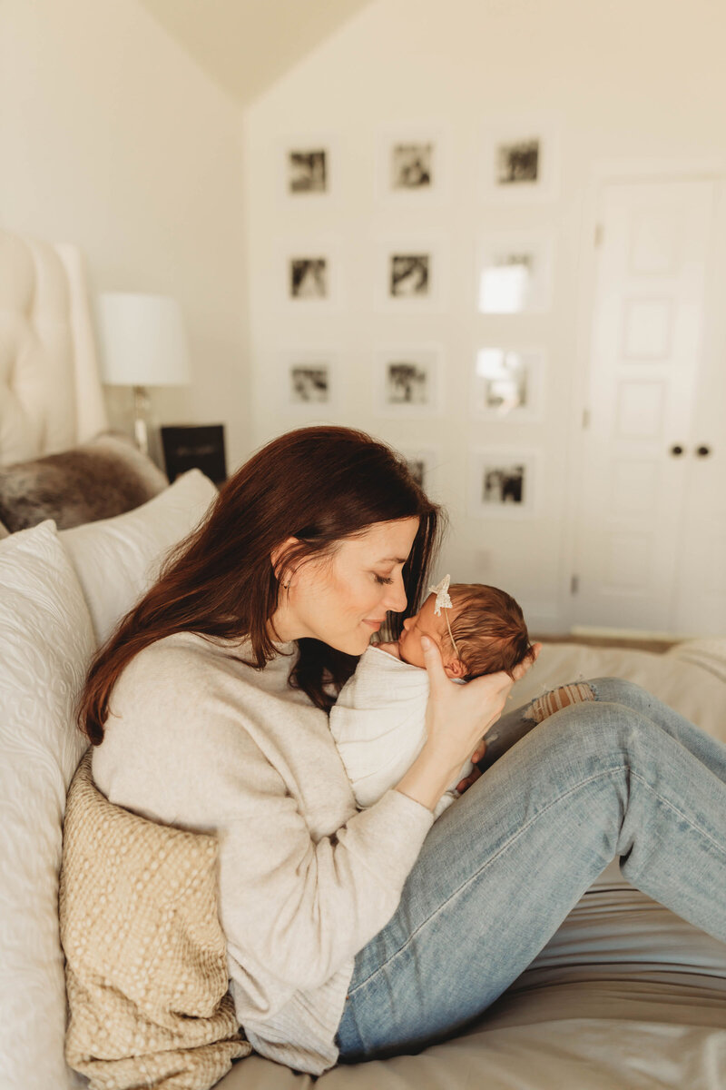 brunette mother rubbing noses with her newborn baby on a bed