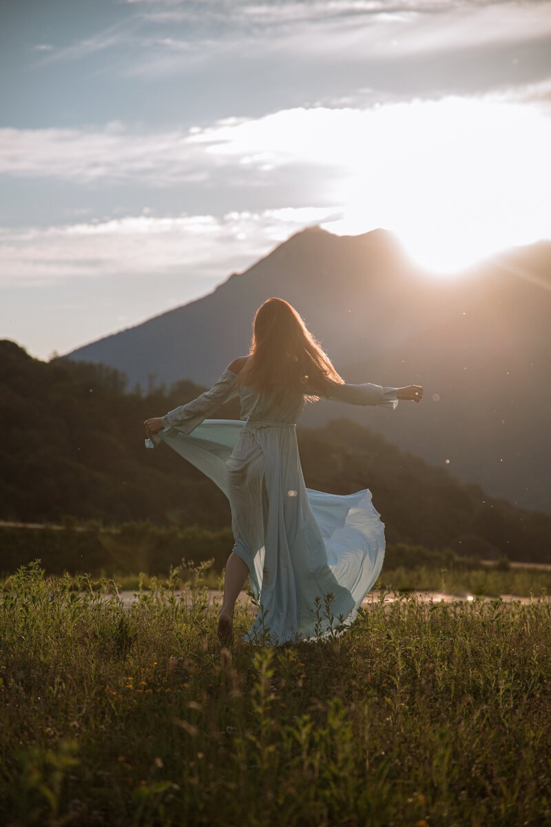 Woman celebrating a life transition by dancing in a field as the sun sets