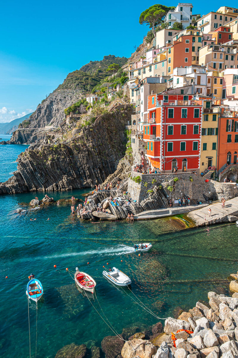 Colorful cliffside houses of Riomaggiore in Cinque Terre, Italy, overlooking turquoise water with boats and swimmers