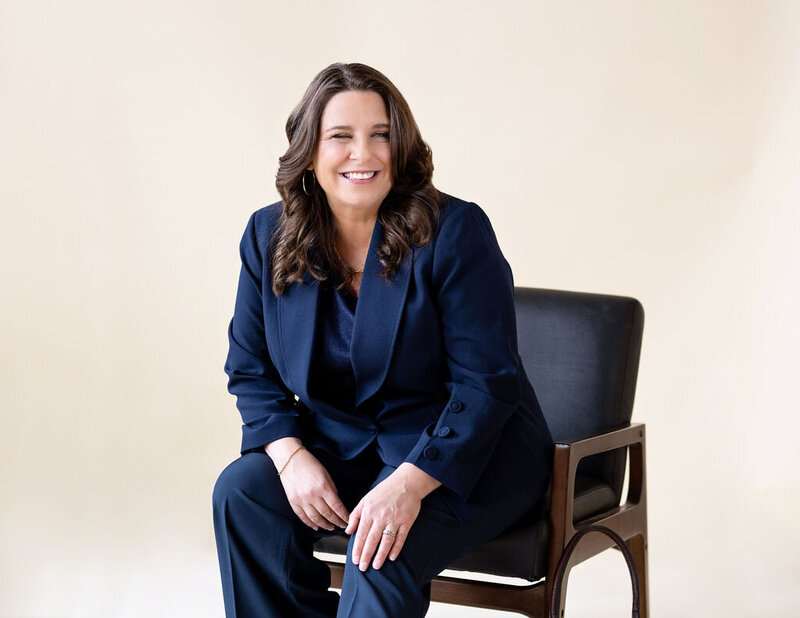 Dr. Chris Limone standing confidently in a navy blazer, holding a phone with flowers in the background
