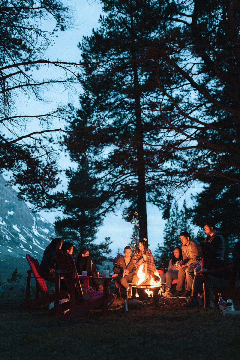 newlyweds and their friends sitting around a campfire after eloping in baff national park in canada