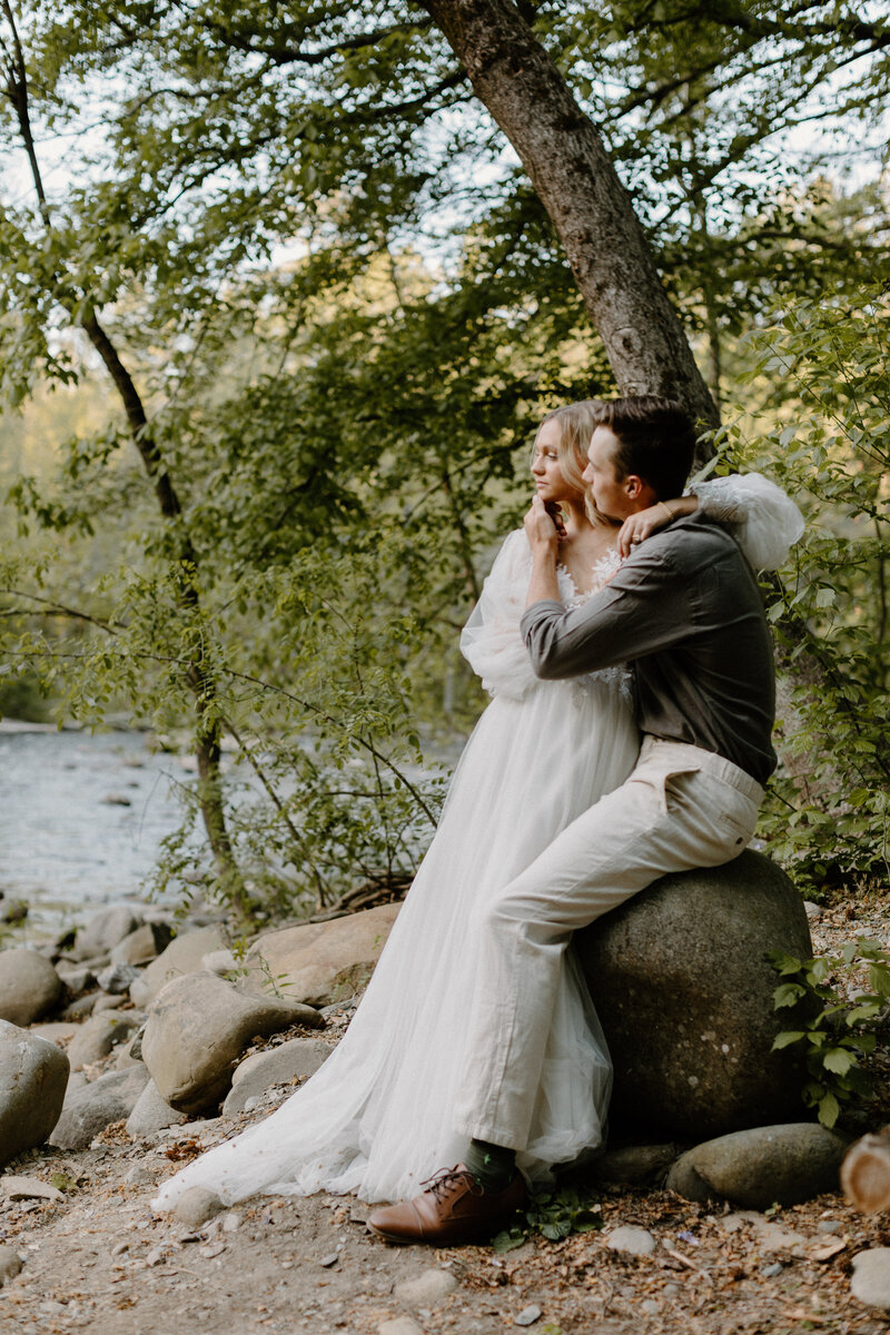 bride and groom sitting on a rock along a creek in the forest