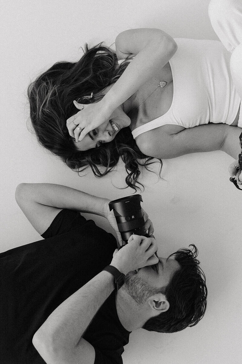 Wedding photographer and videographer based in Minnesota lay on the floor taking photos of each other