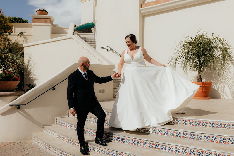 Groom helps the bride down the stairs on their wedding day at Arizona Grand Resort