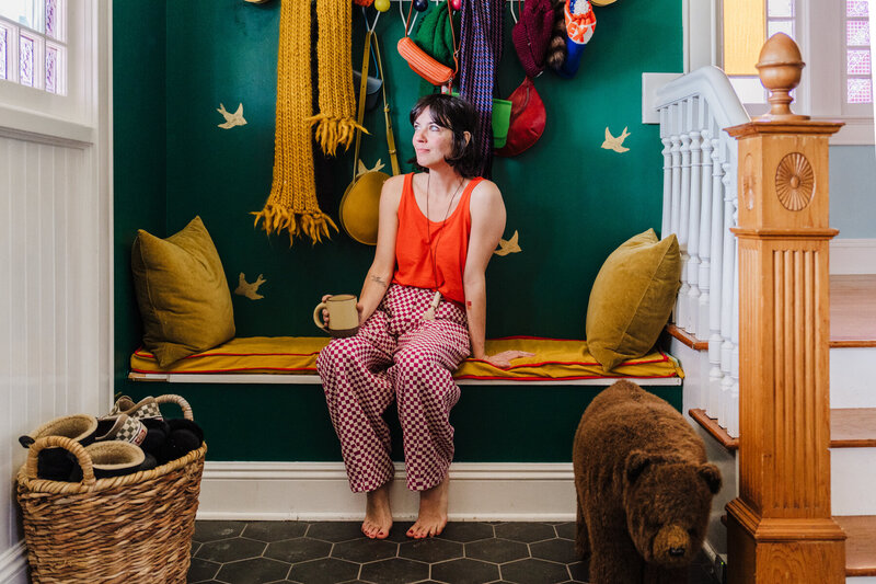 woman in colorful outfit sits against her foyer