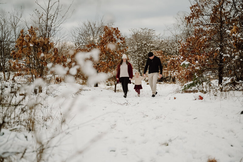 Mom, dad, and 3 year old daughter walking in the snow in Severn Maryland