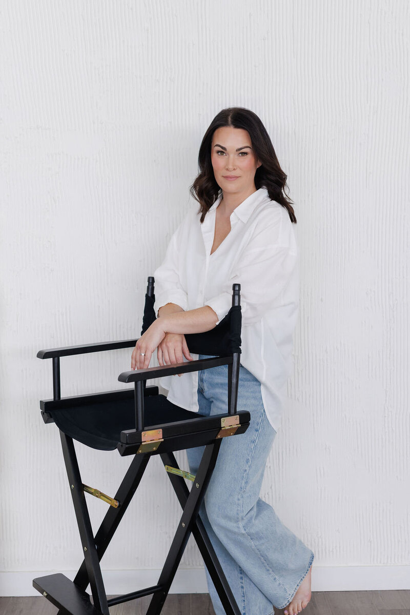 Owner, Courtney Elizabeth, sitting and smiling at the camera. She is wearing a white top and light jeans