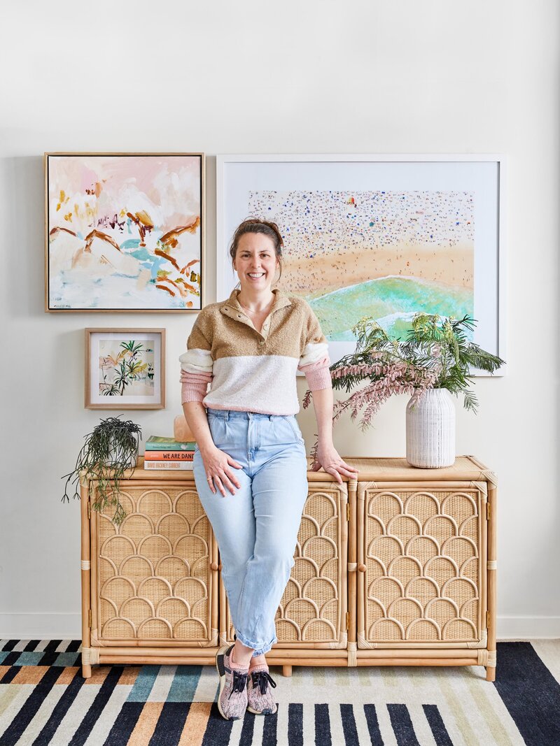 Lisa Hunter, Melbourne interior stylist, photographed in styled living space with artwork and rattan sideboard.