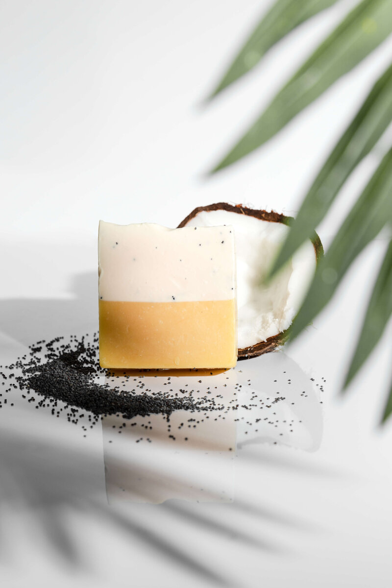 Product photo of soap with a coconut and seeds with a leaf in the foreground